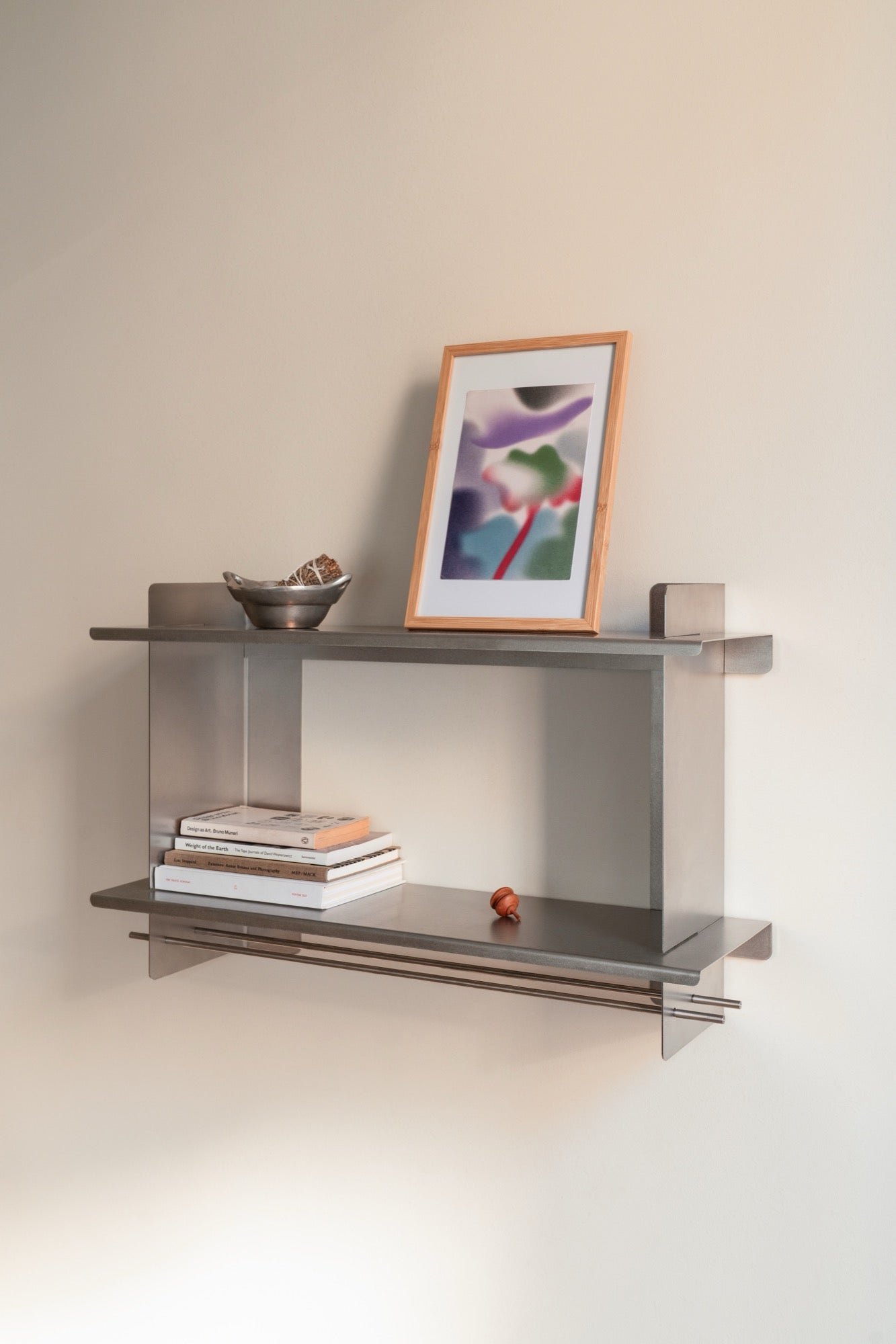 the Tivo Shelf Short in stainless steel mounted on a white living room wall storing books and art